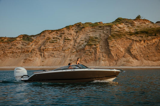 Four Winns H4 Horizon bowrider cruising along rocky shoreline with Mercury outboard – available at Lark Marine, Northern Michigan